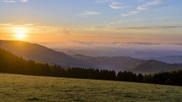 Sonnenaufgang über einem Feld mit Hügeln im Hintergrund auf dem Uplandsteig im Sauerland