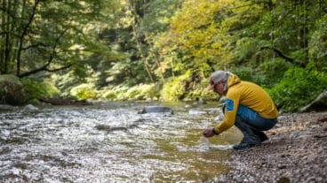 Ein Wanderer hockt am Fluss Alb auf dem Albsteig Schwarzwald und schöpft Wasser mit den Händen