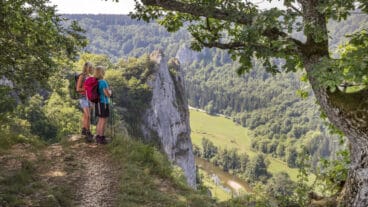 Zwei Wanderer stehen auf dem Gipfel des Stiegelesfelsens und blicken ins Donautal mit dem Fluss darunter