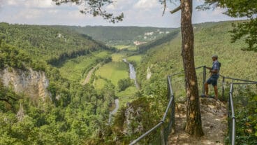Ein Wanderer steht auf dem Gipfel des Knopfmacherfelsens und blickt ins Donautal auf den Fluss darunter